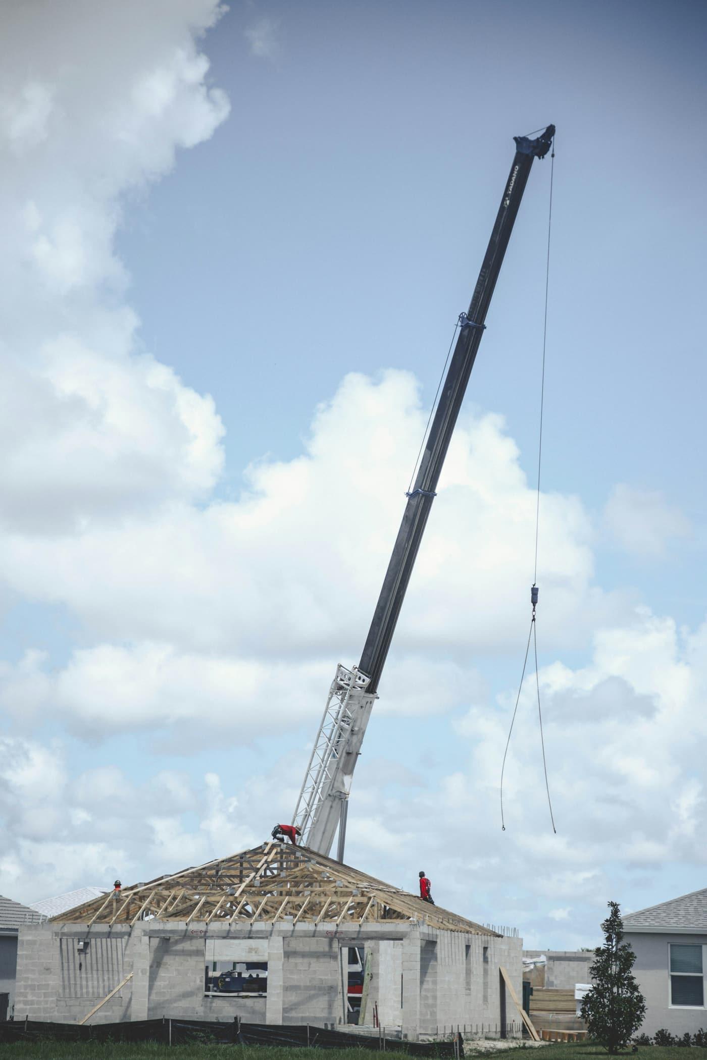 Mobile crane lifting a roof structure onto a single-storey building under a cloudy sky