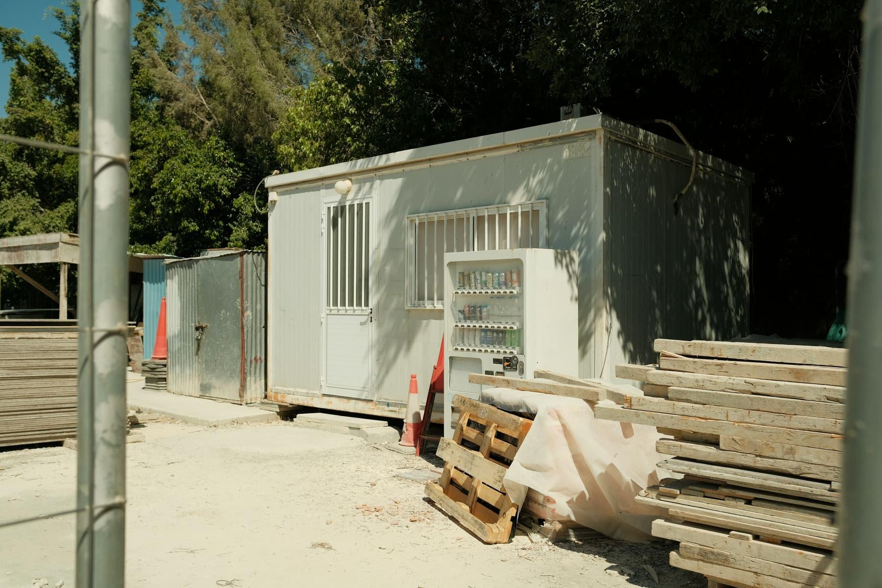 White portable building on a construction site next to stacked timber and pallets