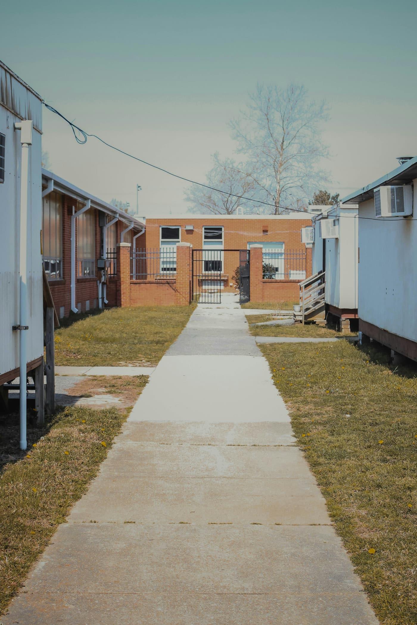 Concrete walkway between two rows of portable classroom buildings leading to a brick school building